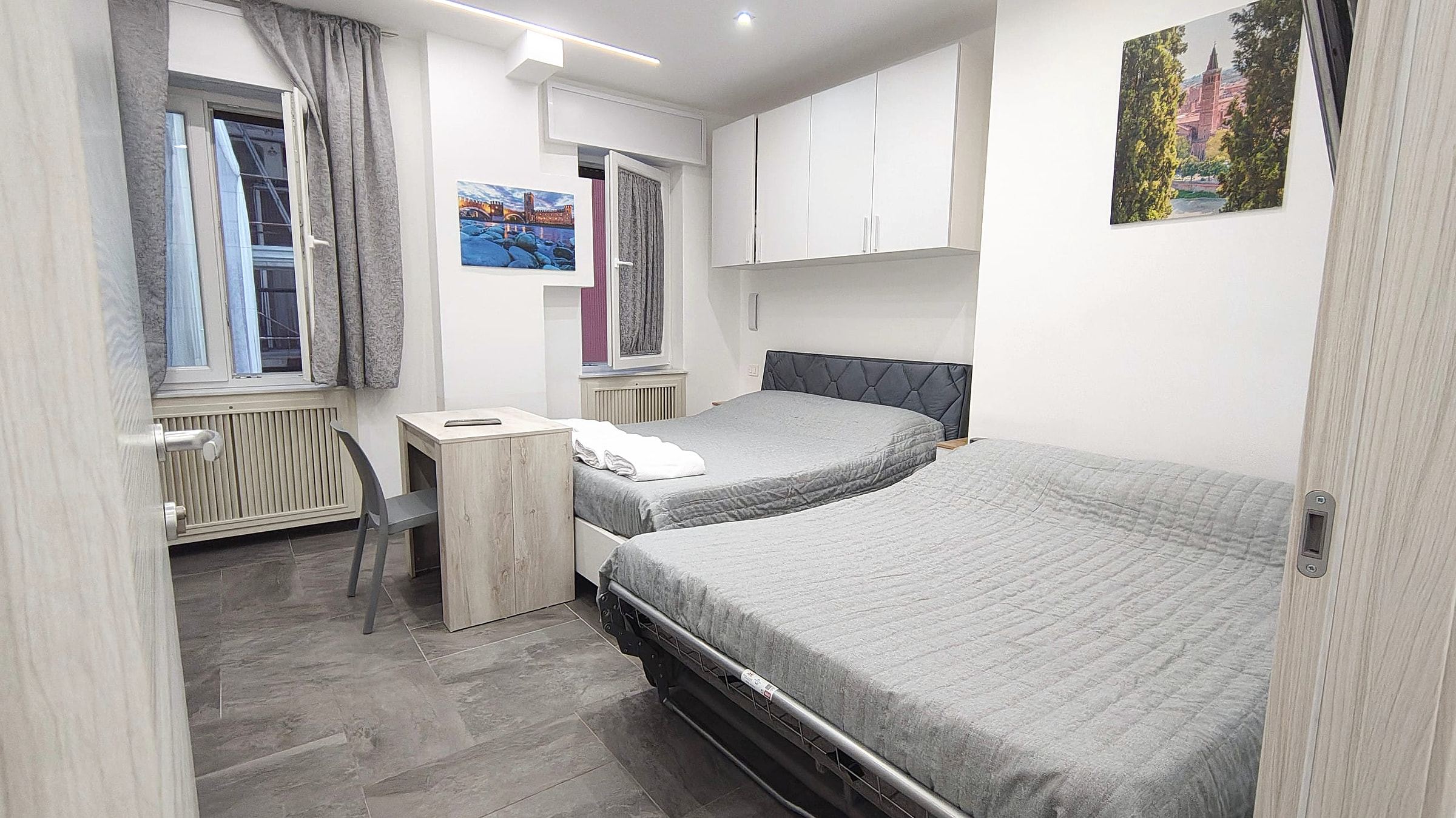 Camera quadrupla con divano letto aperto accanto al letto matrimoniale e scrivania in rovere chiaro