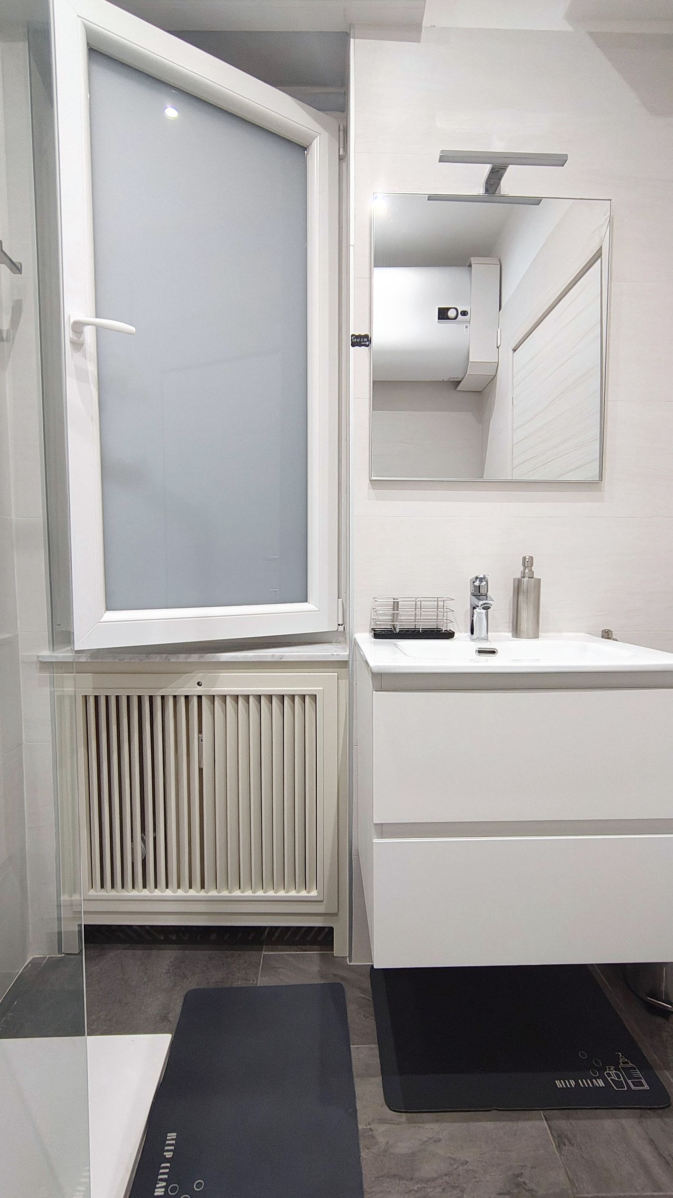 Lavabo sospeso bianco con specchio e applique nel bagno privato con piastrelle chiare