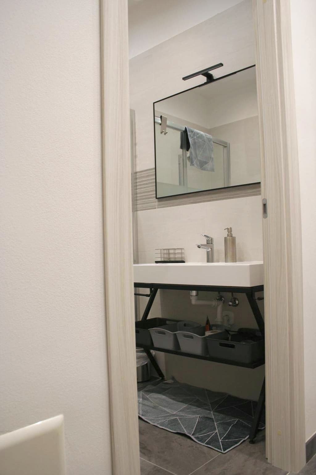 Lavabo bianco su struttura metallica nera con specchio nel bagno del monolocale