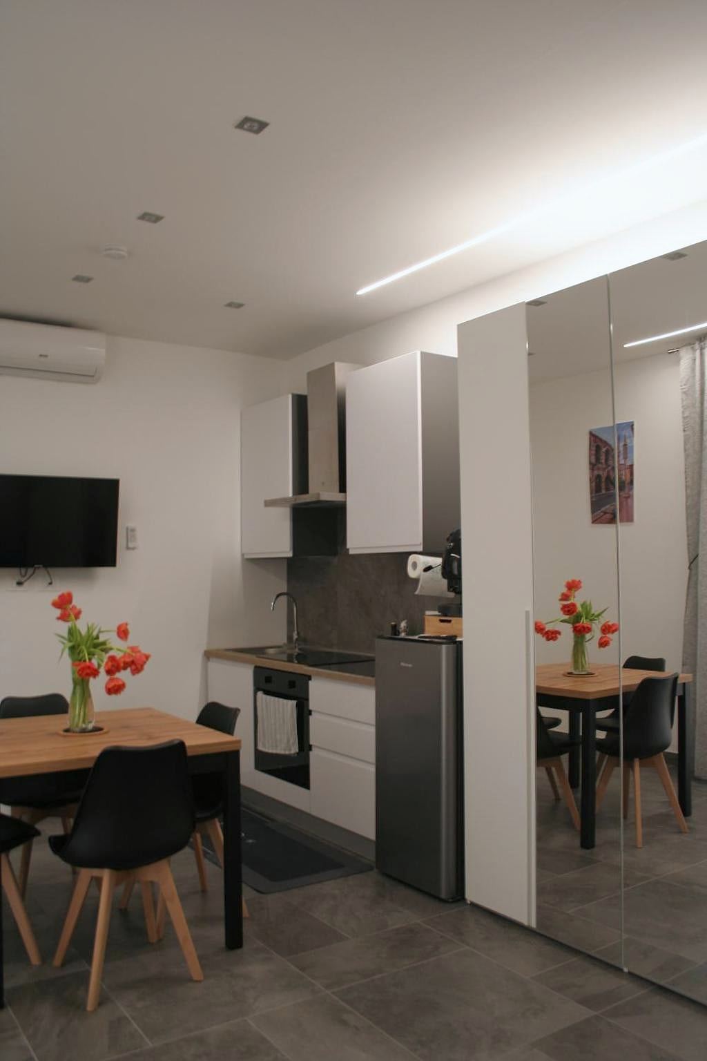 Cucina bianca con frigorifero, tavolo e sedie nere e televisore nel monolocale