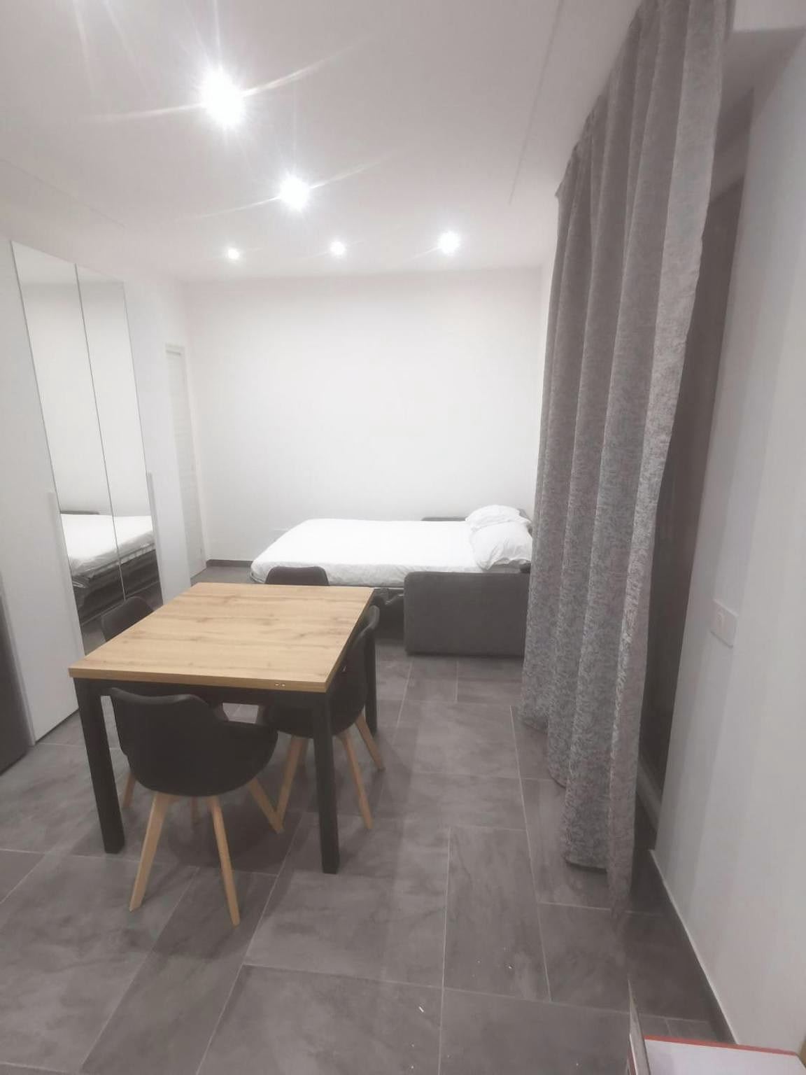Divano letto aperto accanto a una tenda grigia nel monolocale