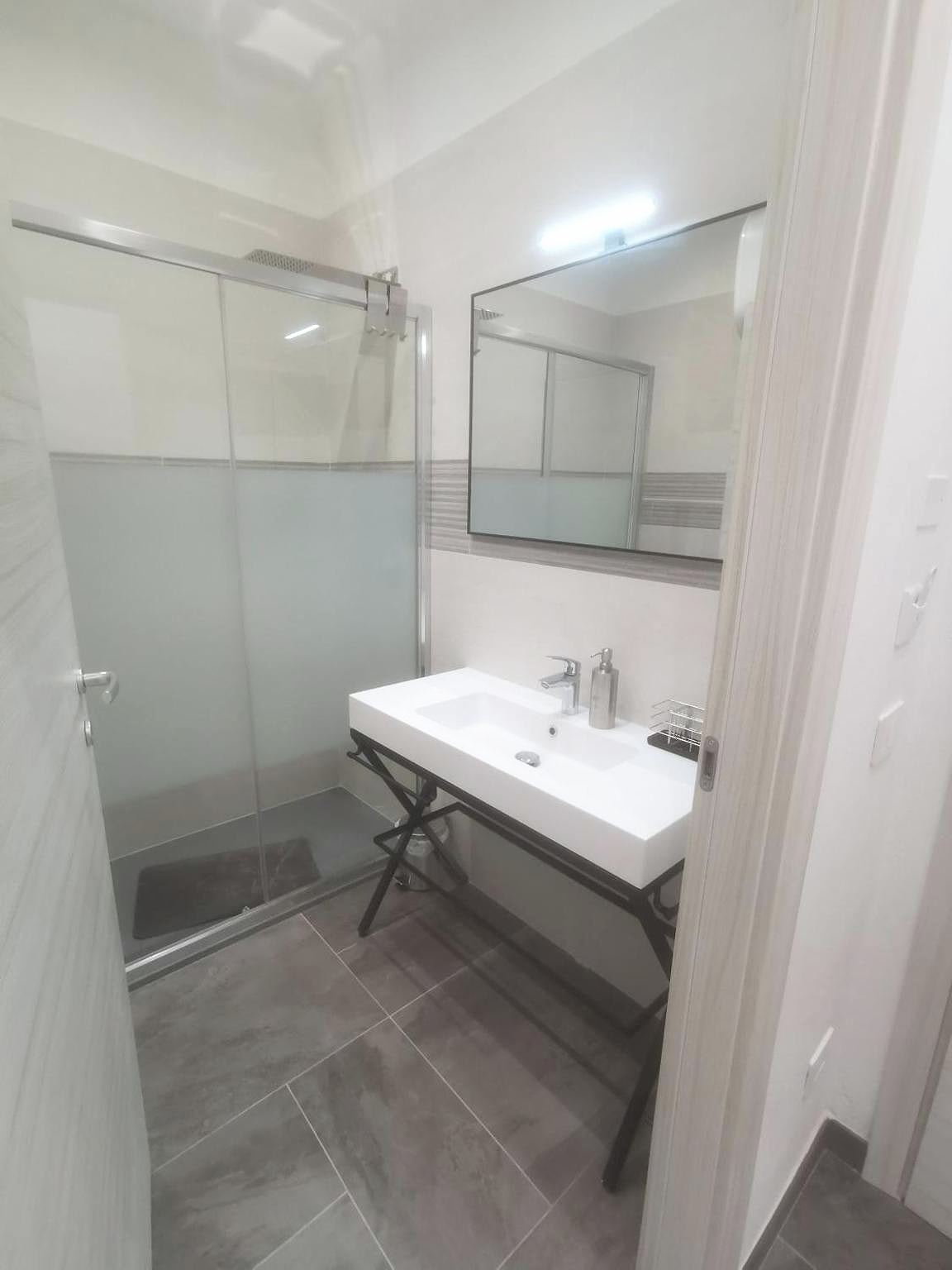 Bagno del monolocale con doccia a vetro satinato e lavabo bianco con specchio illuminato a LED